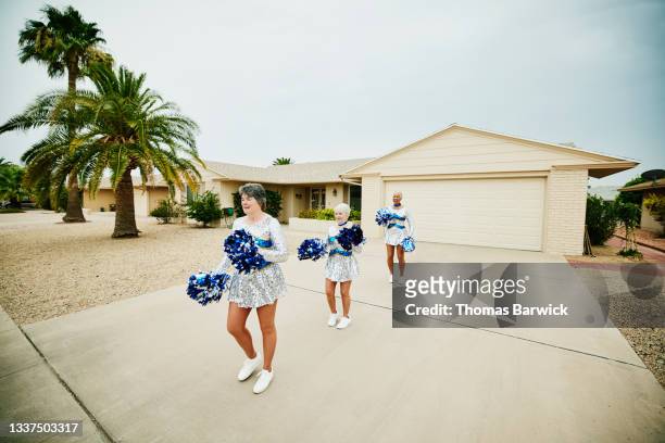 Extreme wide shot of senior female cheerleaders practicing in driveway of home on summer morning