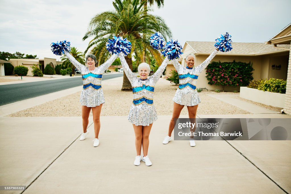 Wide shot of senior female cheerleaders practicing in driveway on summer morning