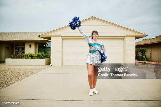 Wide shot portrait of smiling senior female cheerleader posing in front of home