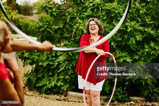 Medium shot of laughing mature woman exercising with spinning plastic hoop in backyard