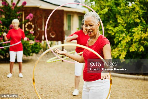 Medium shot of smiling senior female dance group practicing with spinning plastic hoops in backyard