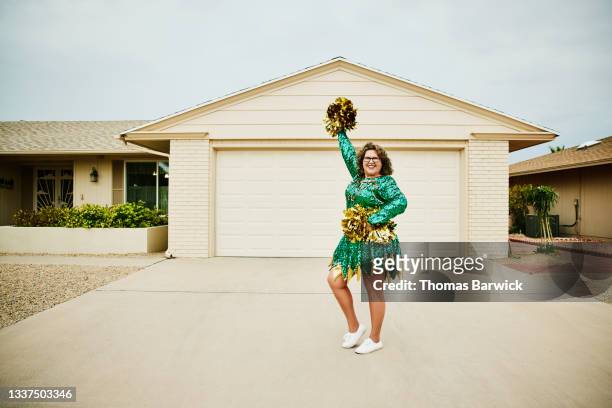 Wide shot portrait of smiling mature female cheerleader posing in front of home