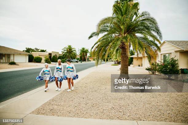 Extreme wide shot of senior female cheerleaders walking on sidewalk in neighborhood