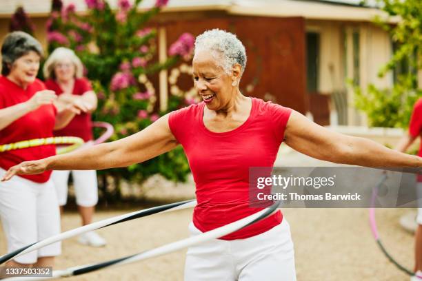 medium shot of smiling senior female dance group practicing with spinning plastic hoops in backyard - active seniors stockfoto's en -beelden