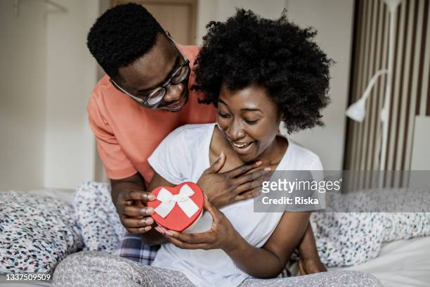 young man surprising his girlfriend with a love present in the morning - valentines african american 個照片及圖片檔