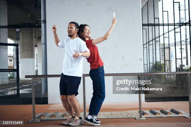 a young couple dancing to music with their cell phones in the park. - 喜ぶ ストックフォトと画像