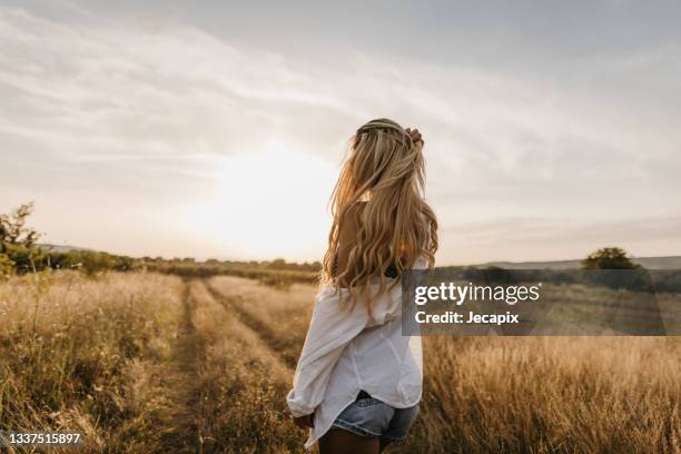 back view of long haired woman standing in grass field and looking away - long hair stock pictures, royalty-free photos & images