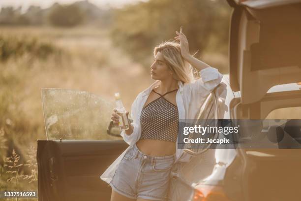 femme appuyée sur une voiture dans la nature tout en tenant une cigarette et une bouteille de cidre dans les mains - cidre photos et images de collection