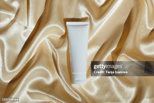 white tube bottle with moisturizer on silk fabric beige background. beauty products. skin care concept. - creme tube ストックフォトと画像