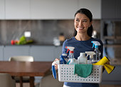 Happy woman at home holding a basket of cleaning products