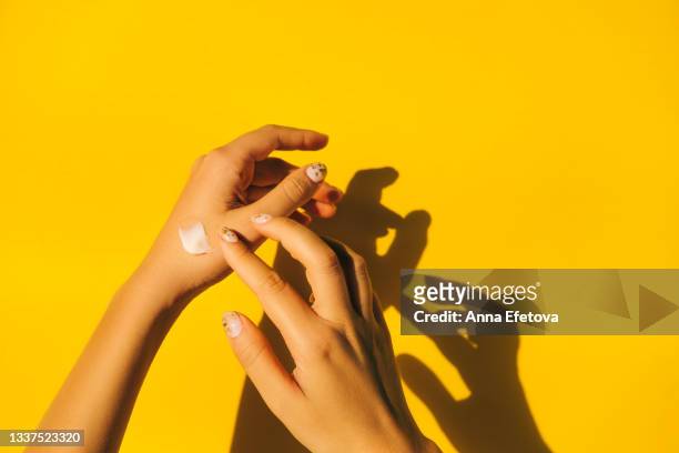woman is spread cream on hands with manicure against illuminating yellow background. body care concept. trendy colors of the year 2021. flat lay style - cream stock pictures, royalty-free photos & images
