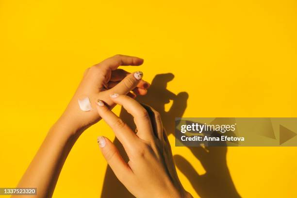 woman is spread cream on hands with manicure against illuminating yellow background. body care concept. trendy colors of the year 2021. flat lay style - cream coloured imagens e fotografias de stock