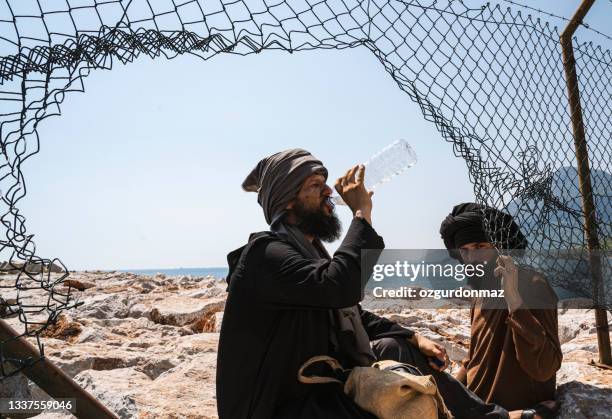 two male refugee men sitting under the fence - beach bum stock pictures, royalty-free photos & images