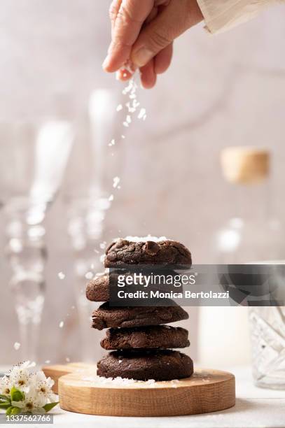 stack of chocolate cookies on wooden board with human hand placing sea flakes on top - sea salt stock pictures, royalty-free photos & images