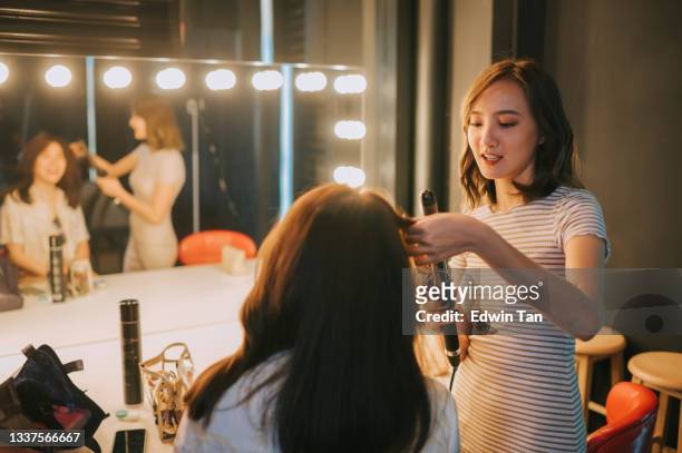 asian chinese female make up artist doing hairdo for her customer in makeup room illuminated with led lamp in front of mirror - hair coils stockfoto's en -beelden