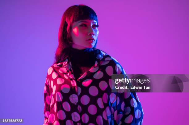 waist up neon blue purple lights posing in studio asian chinese female fashion model with polka dot blouse in studio portrait looking away - gel effect lighting stock pictures, royalty-free photos & images