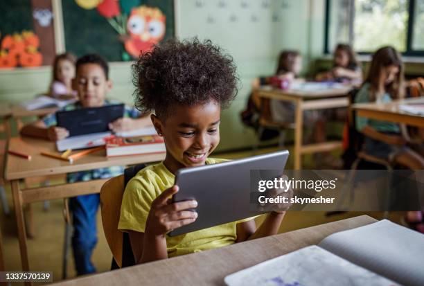 happy black elementary student using touchpad on a class. - students computer imagens e fotografias de stock