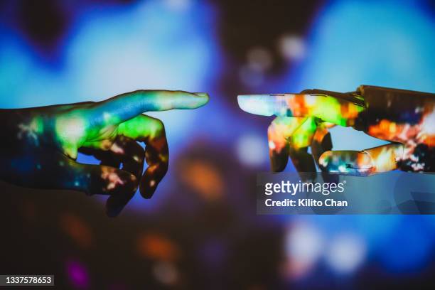 human hand reaching for robotic hand with outer space image projected on it - erschaffung stock-fotos und bilder