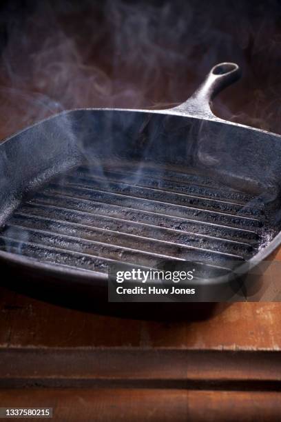 smoking cast iron griddle pan on a dark wooden table - frying pan stock-fotos und bilder