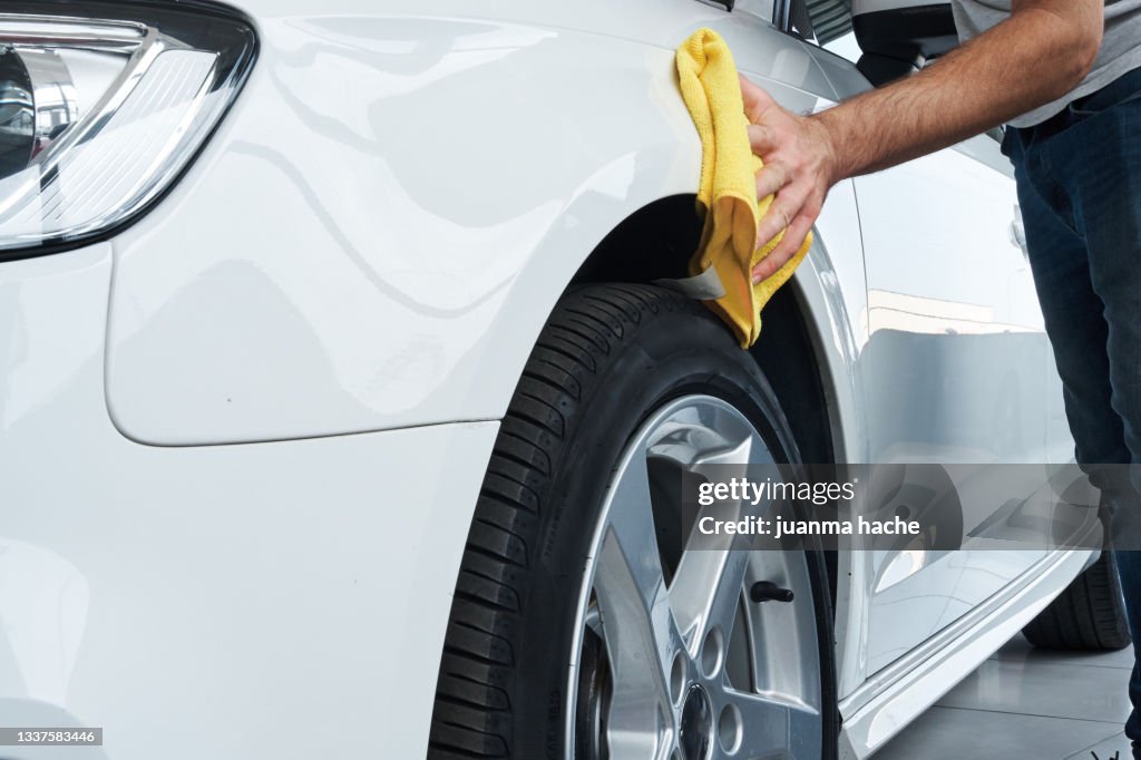 Close up view of a worker detailing polishing a white car with a rag.
