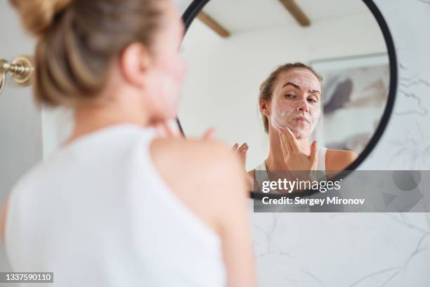young woman applying mask on face - facial cleanser stockfoto's en -beelden
