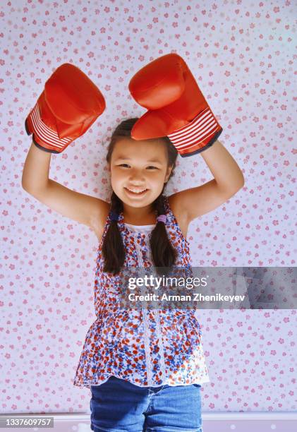 mischievous  girl wearing boxing gloves with her arms raised against the wallpapered wall - funny boxing stock-fotos und bilder