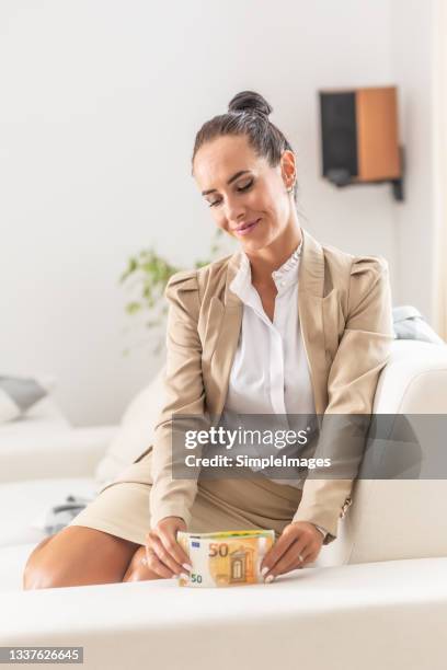 satisfied woman holds a bunch of euro notes aligning them on a sofa she sits on. - fondsmanager stock-fotos und bilder