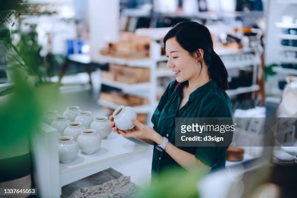 young asian woman shopping for household necessities in a homeware store looking at a ceramic plant pot - furniture store stockfoto's en -beelden