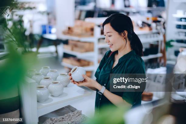 young asian woman shopping for household necessities in a homeware store looking at a ceramic plant pot - department store stock pictures, royalty-free photos & images