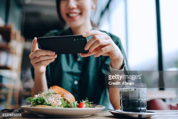 joyful young asian woman taking photos of delicious lobster salad brioche bun with bamboo charcoal black and white colour coffee with smartphone before eating it in cafe. eating out lifestyle. camera eats first culture - fine dining food stock-fotos und bilder
