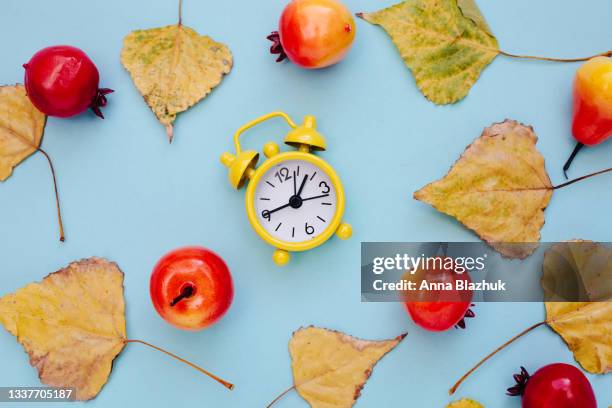autumn yellow leaves over blue background. yellow retro alarm clock. - orange alarm clock stock pictures, royalty-free photos & images