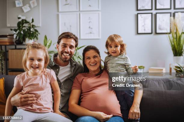 ritratto di famiglia a casa, seduto sul divano con due figlie. la donna è incinta - famiglia con due figli foto e immagini stock