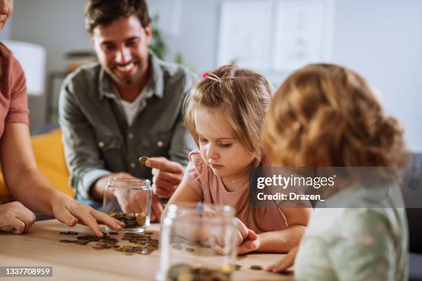 töchter mit vater und mutter, die münzen aus dem glas zählen - couple saving piggy bank stock-fotos und bilder