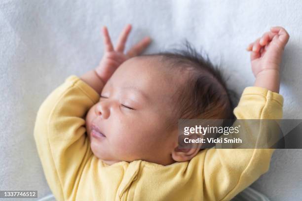 close up photo of a one week old baby boy with dark hair , asleep with arms over head, mixed race, asian and caucasian. - newborn sleeping stock pictures, royalty-free photos & images