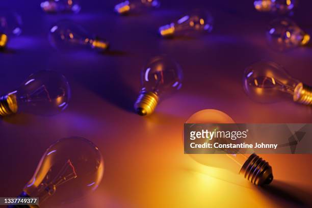 group of scattered light bulbs with one uniquely switched on and illuminating the space - idea bulb stockfoto's en -beelden