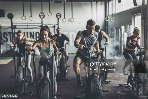 entraînement de cross fit sur des vélos stationnaires dans une salle de sport! - cours de spinning photos et images de collection