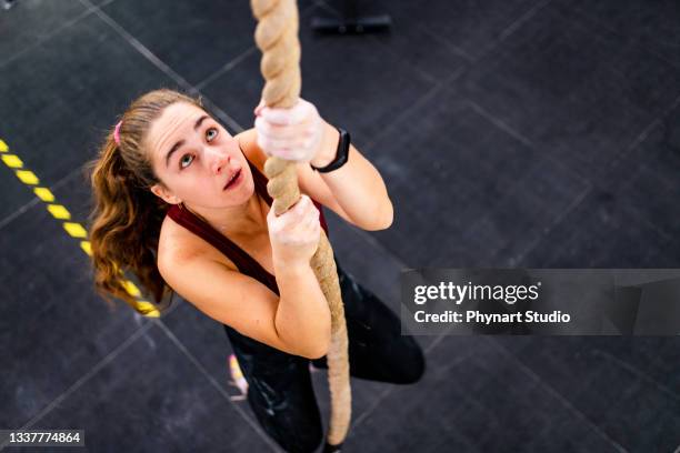 entschlossene athletische frau, die in einem fitnessstudio das seil hinaufzieht - zäh stock-fotos und bilder