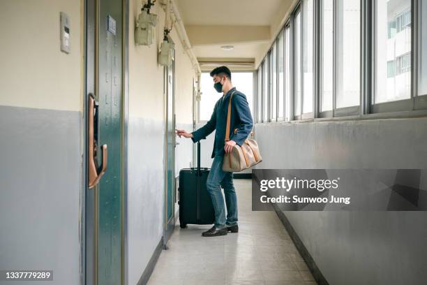 side view of young man with suitcase opening door - motel stock-fotos und bilder