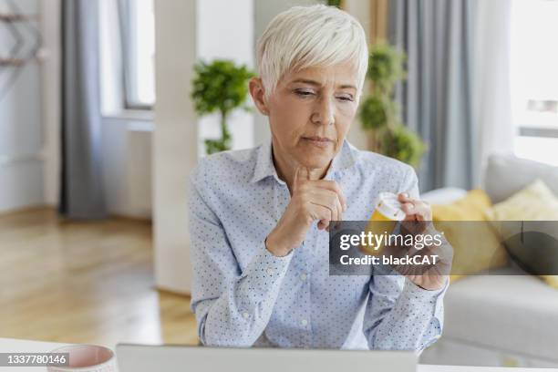 worried senior woman holding a bottle of medicine in her hand - taking medication stockfoto's en -beelden