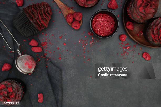 image of black, metal wire cooling rack with rows of homemade, chocolate cupcakes in brown, paper cake case, chocolate butter icing piped swirl coated with dehydrated raspberry dust, sieve, wooden spoon, black background, elevated view - cake case stock pictures, royalty-free photos & images