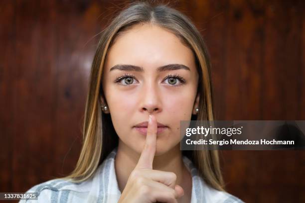 young latino woman with green eyes looking at the camera with a finger on her lips, asking for quiet, silence - woman with finger on lips stock pictures, royalty-free photos & images