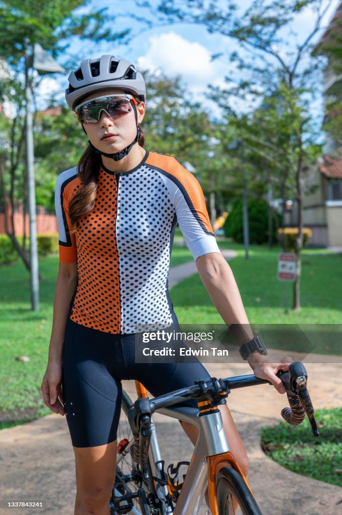 Portrait d’une cycliste chinoise asiatique regardant l’appareil photo avec une attitude cool au parc public avec son vélo de route