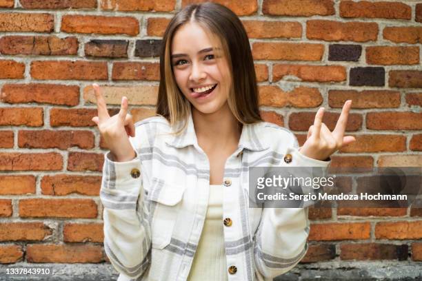 latino woman looking at the camera and doing the heavy metal horns hand sign - glam rock stock pictures, royalty-free photos & images