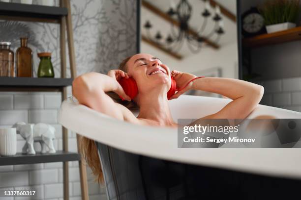 woman lying in bathtub and enjoys music in red headphones - red tub stock pictures, royalty-free photos & images