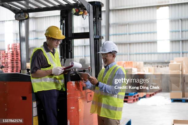 asian chinese warehouse supervisor manager signing documents receiving goods from his coworker operating forklift working in industry factory - loader reading stock pictures, royalty-free photos & images