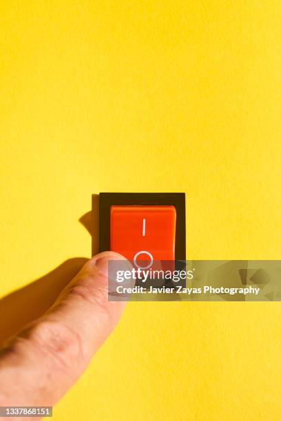 cropped finger switching a rocker switch on a yellow background. power-off position. - encender o apagar fotografías e imágenes de stock