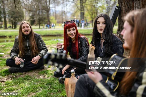 glückliche gothic-freunde, die es genießen, im park mit gitarrenmusik zu trinken - heavy metal stock-fotos und bilder