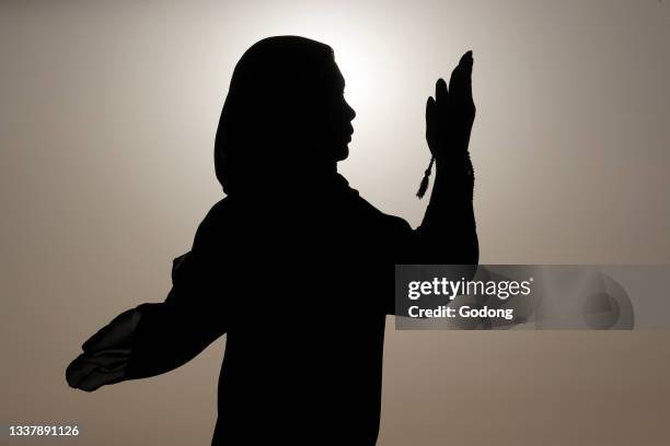 Silhouette of muslim woman holding prayer beads in her hands and praying against the sky. Religion praying concept. United Arab Emirates.