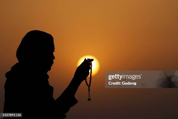 Silhouette of muslim woman holding prayer beads in her hands and praying at sunset. Religion praying concept. United Arab Emirates.