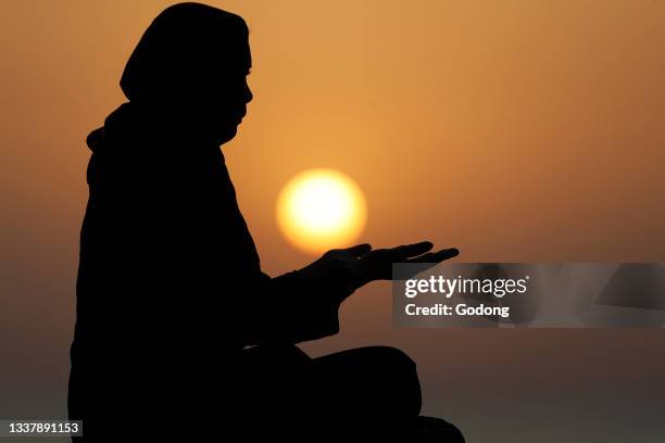 Silhouette of muslim woman in abaya praying with her hands at sunset. Religion praying concept. United Arab Emirates.